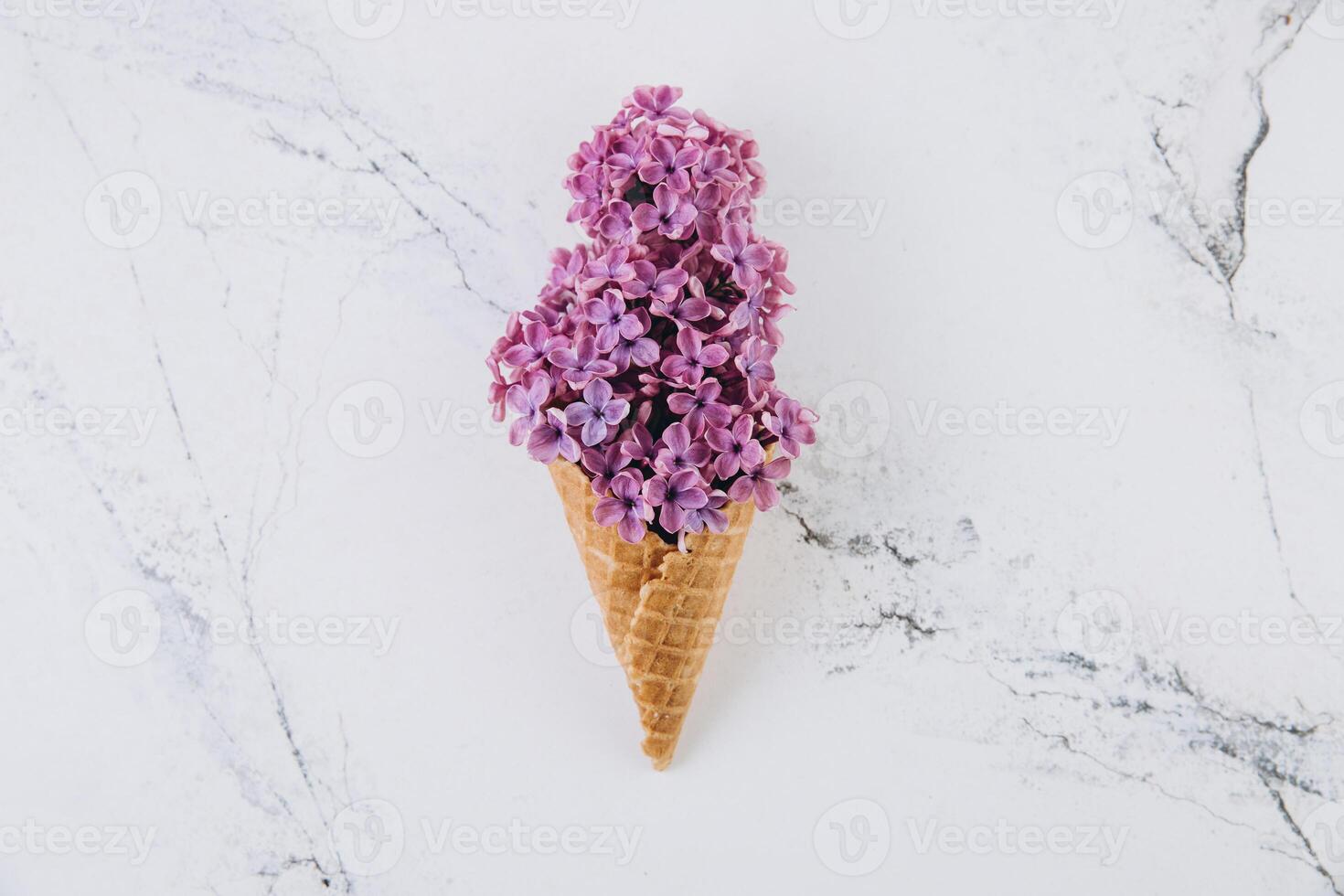 Waffle cone with lilac flower bouquet on marble background. Flat lay, top view, floral and spring composition photo