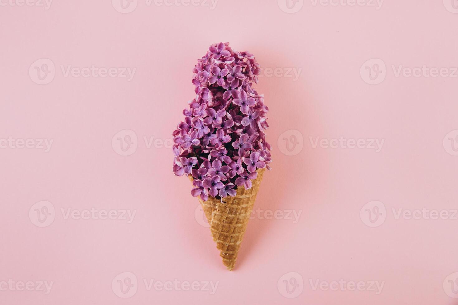 Waffle cone with lilac flower bouquet on pink background. Flat lay, top view. Spring composition photo