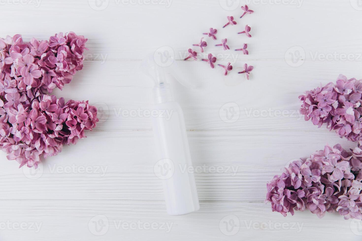 Freshener and floral scent concept. White bottle of perfume with spray of lilac flowers on pink background, flat lay and top view photo