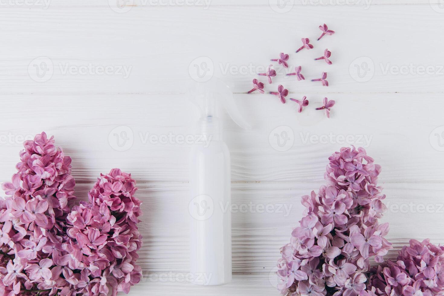 Freshener and floral scent concept. White bottle of perfume with spray of lilac flowers on pink background, flat lay and top view photo