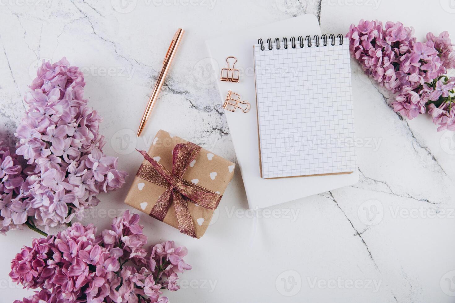 Spring flat lay top view home office workspace - gift and notebook with lilac flowers on a marble desk background photo