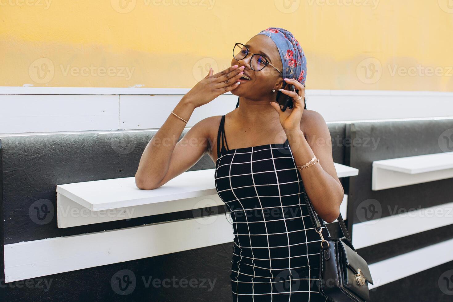 Pretty African American woman in a dress has fun outside and talks by phone photo