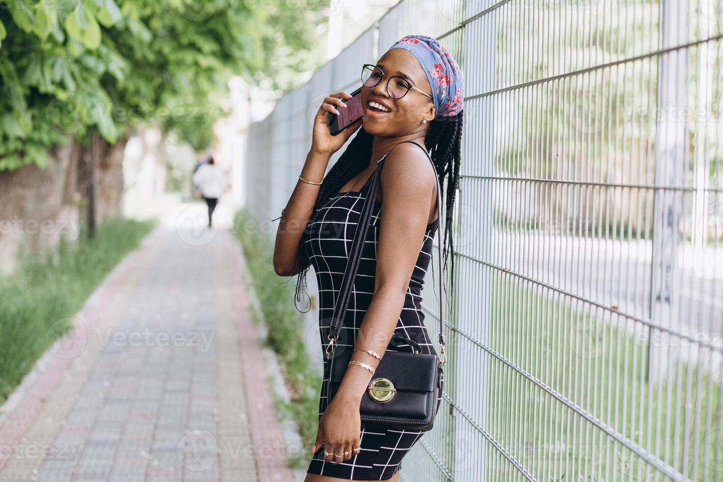 Pretty African American woman in a dress has fun outside and talks by phone photo
