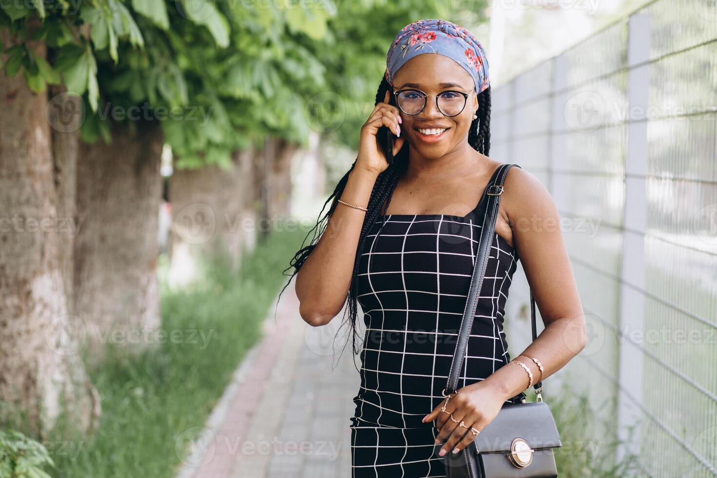 Pretty African American woman in a dress has fun outside and talks by phone photo
