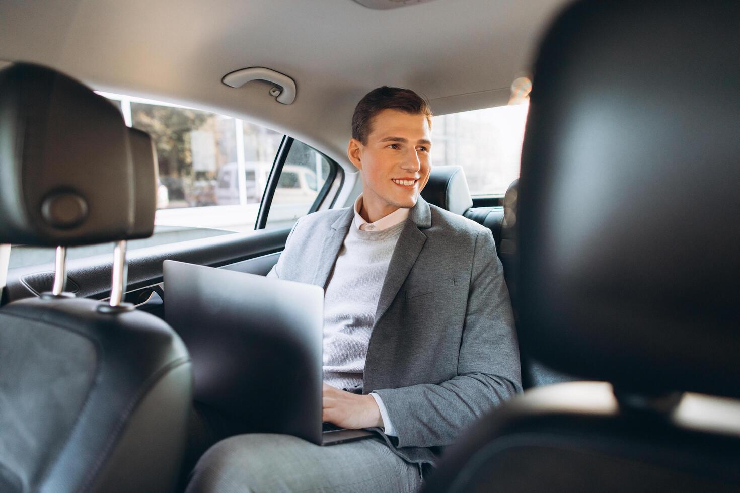 A modern businessman using a laptop computer while sitting in the back seat of a car. photo