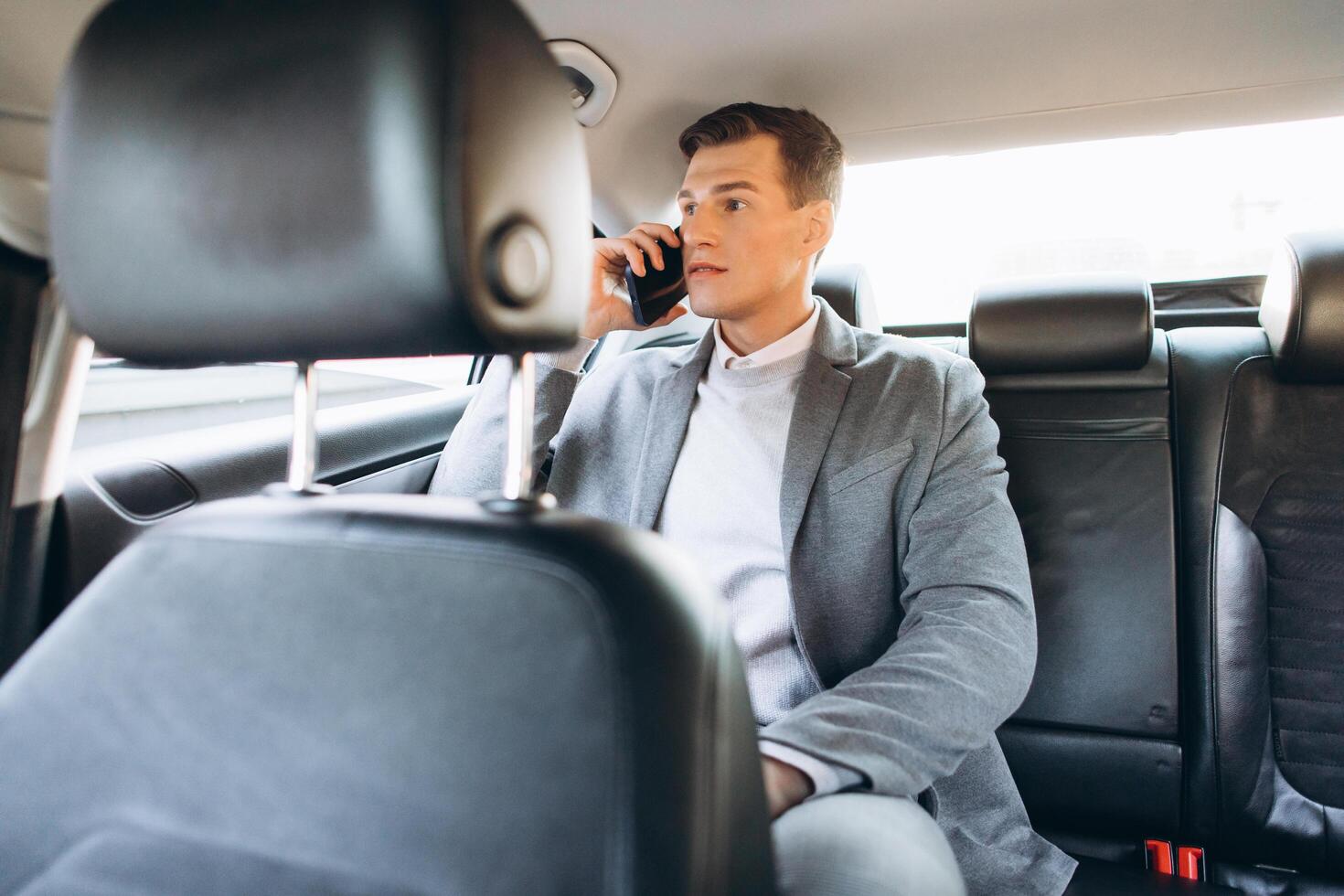 Young businessman talking on a mobile phone while sitting in the back seat of a car. photo