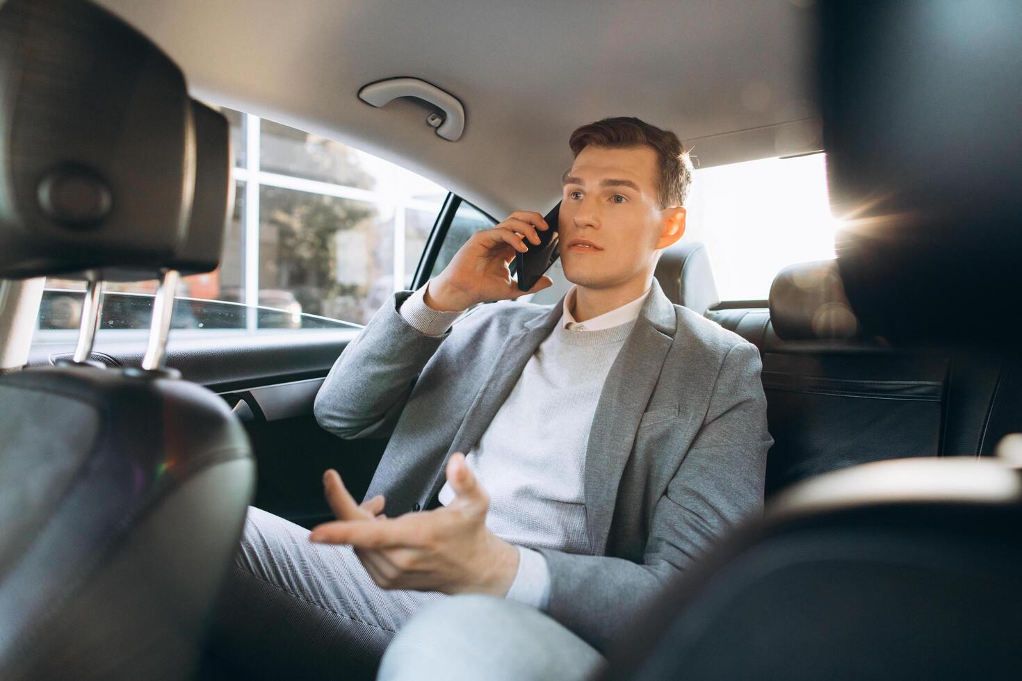 Young businessman talking on a mobile phone while sitting in the back seat of a car. photo