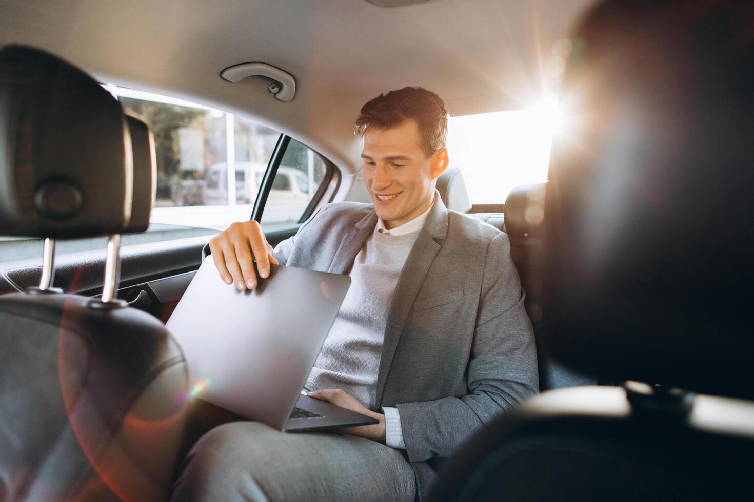 A modern businessman using a laptop computer while sitting in the back seat of a car. photo