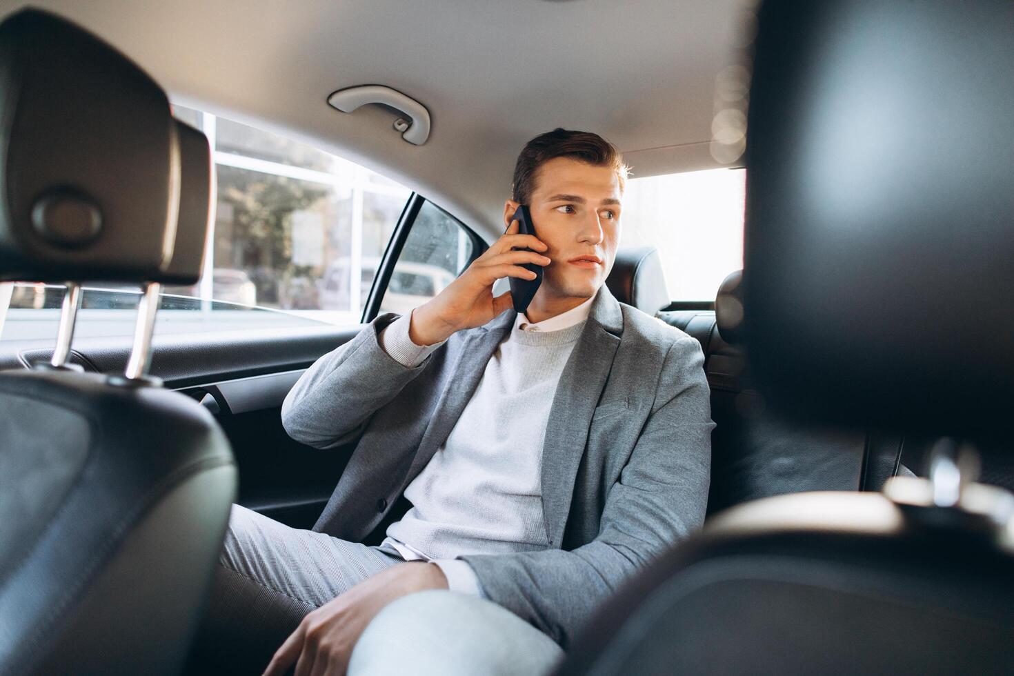 Young businessman talking on a mobile phone while sitting in the back seat of a car. photo