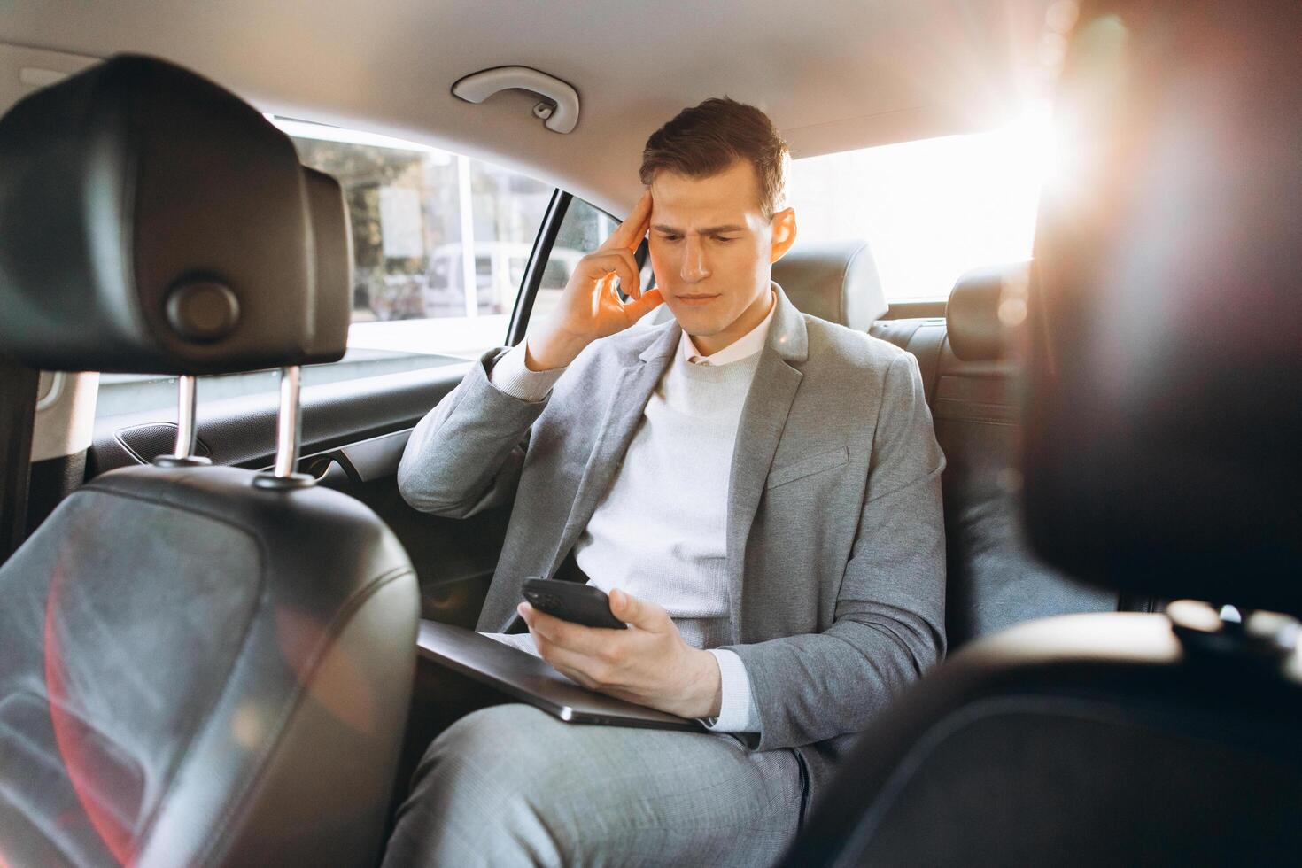 Young businessman tired from work holding hand to his head while sitting in the back seat of the car. photo