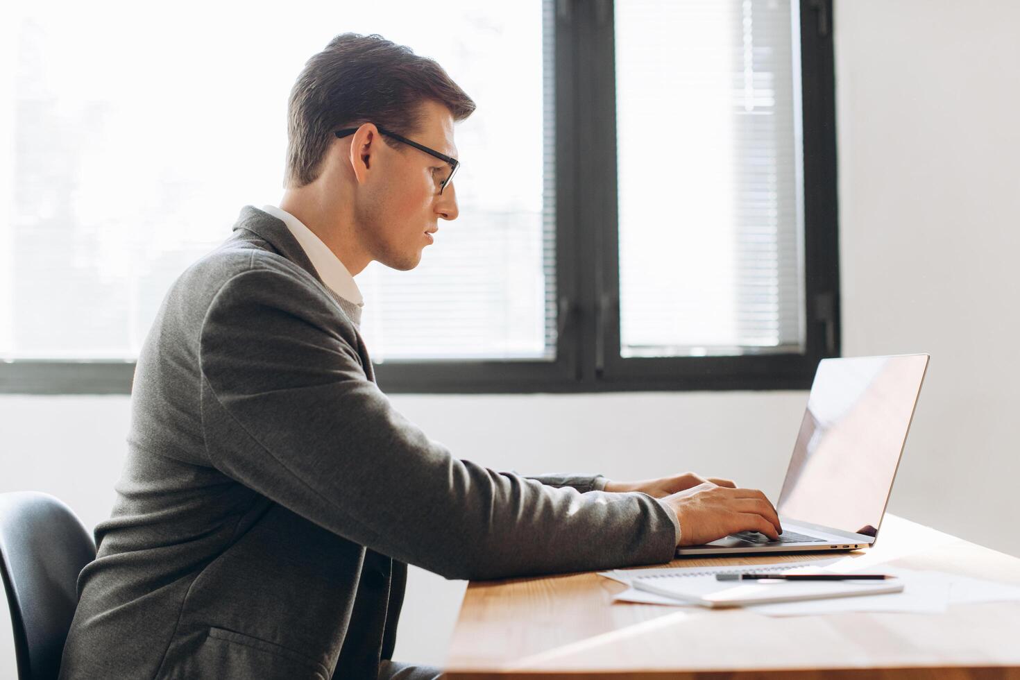 Modern serious man with glasses, office worker working on laptop photo