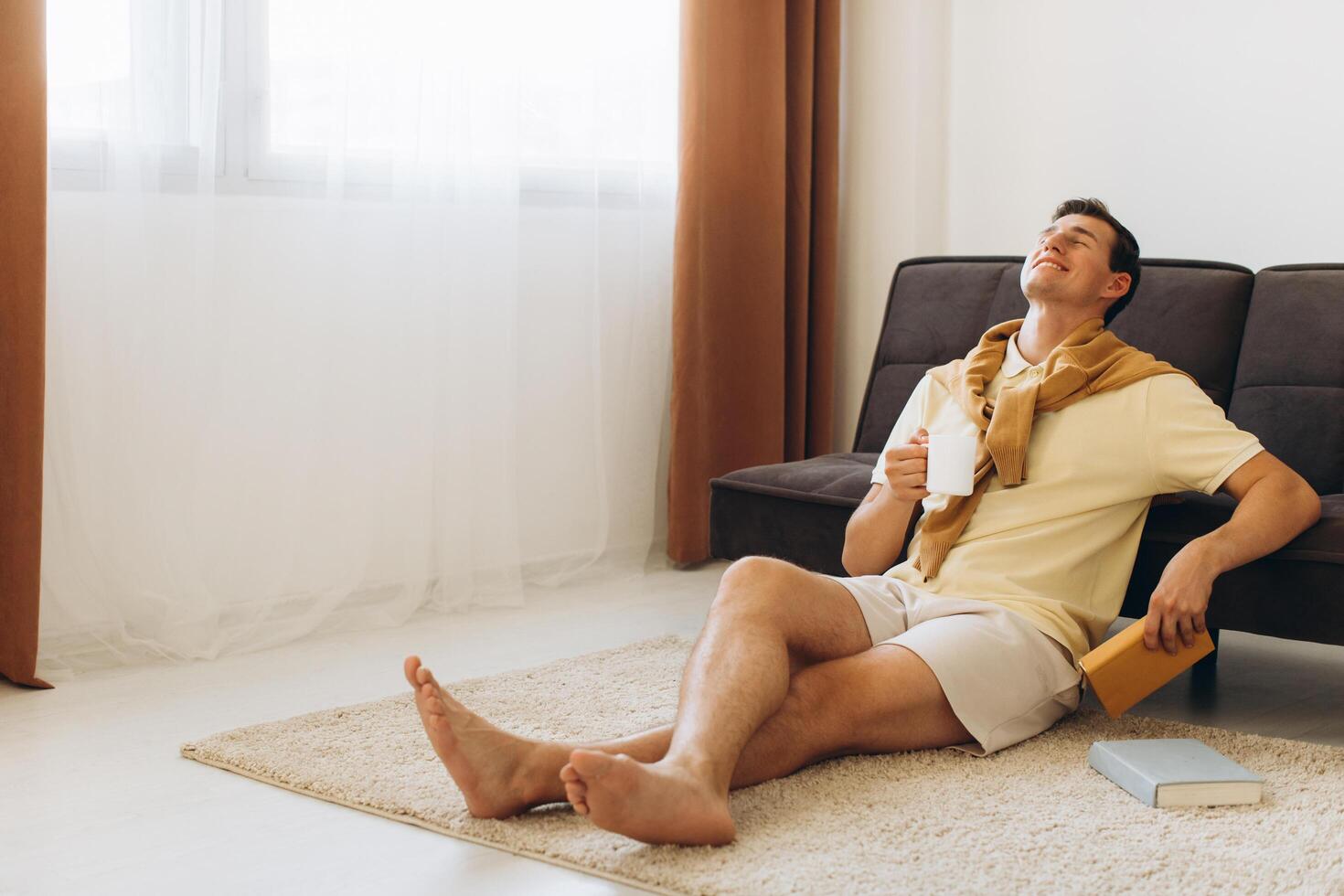 Handsome young man in yellow casual clothes sitting at home reading books and drinking coffee photo