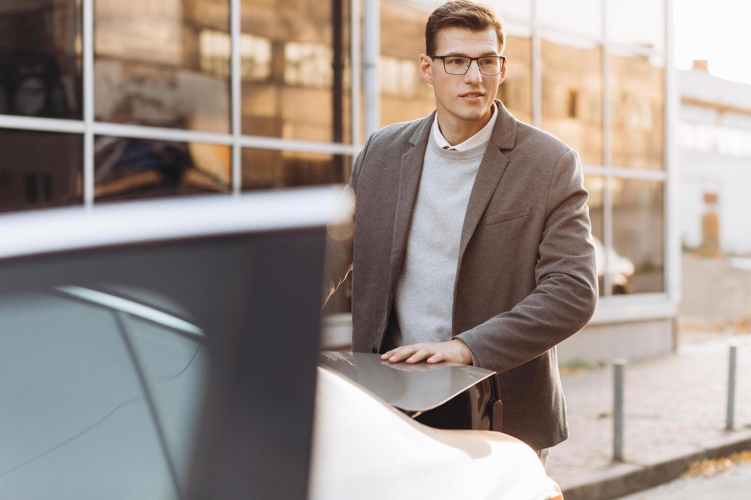 A modern man in glasses opens the trunk of his car photo
