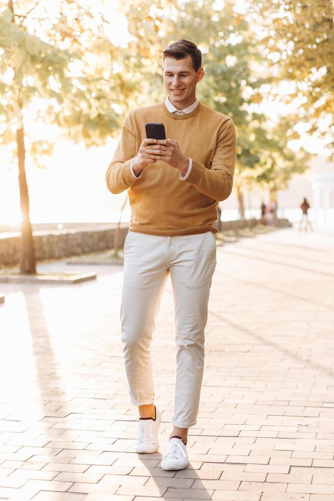 Modern handsome smiling man in yellow and white clothes talking on the phone in the park at sunset photo