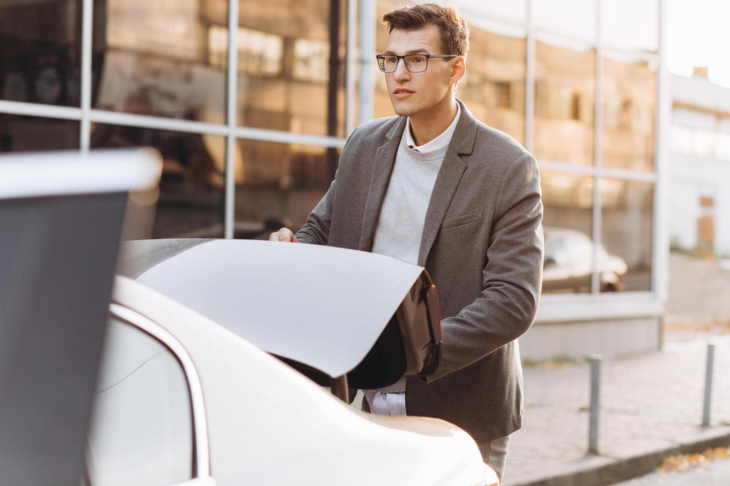 A modern man in glasses opens the trunk of his car photo