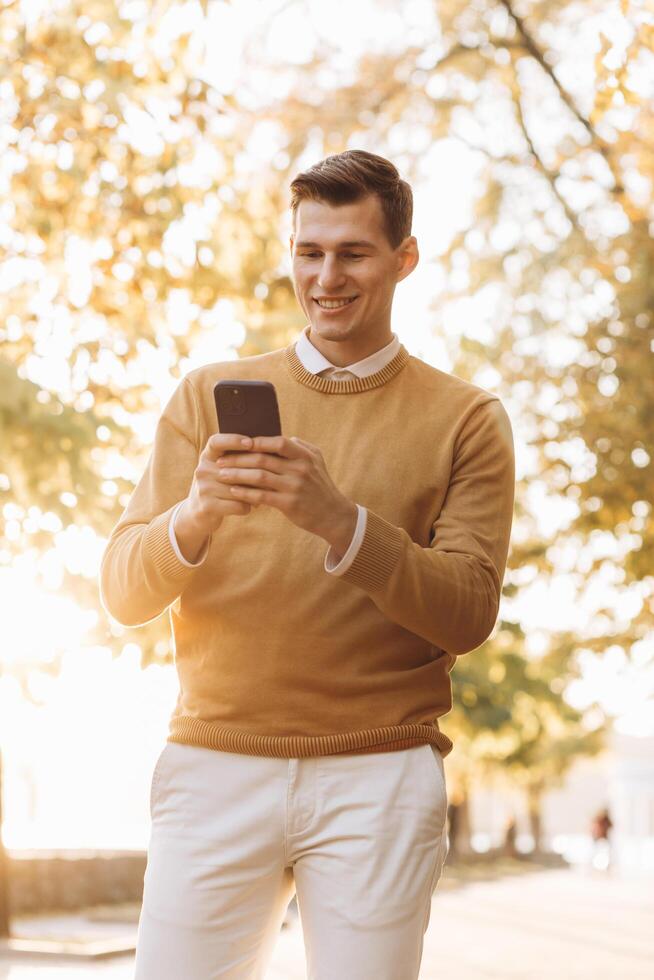 Modern handsome smiling man in yellow and white clothes talking on the phone in the park at sunset photo