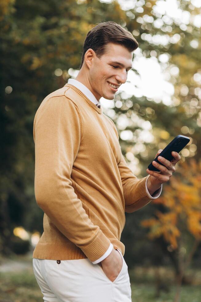 Modern handsome smiling man in yellow and white clothes talking on the phone in the park at sunset photo