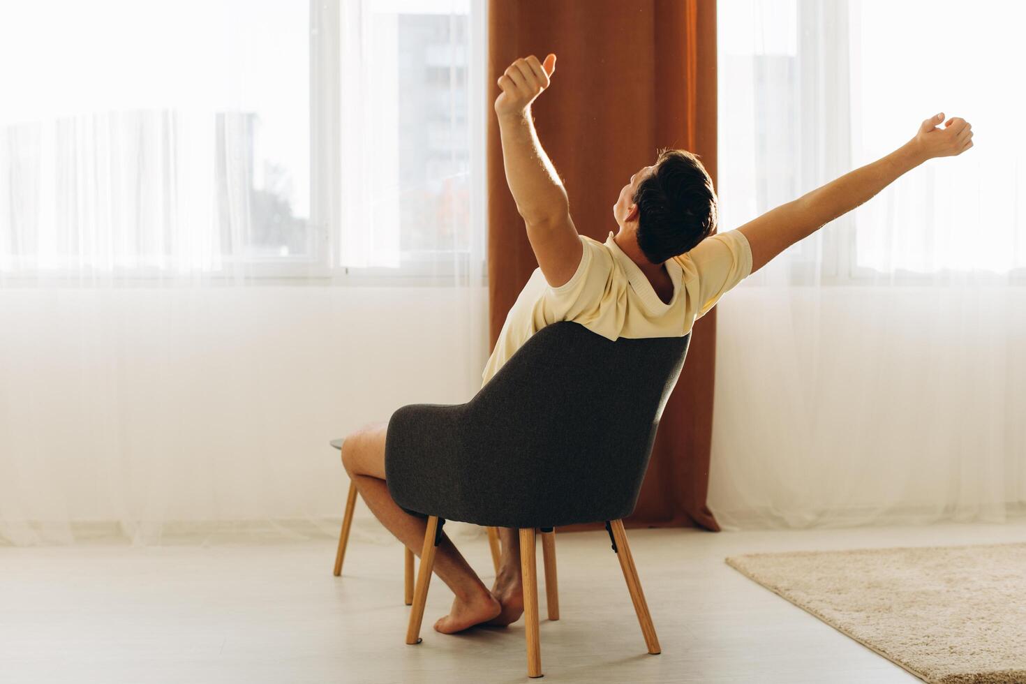 A man at home sits on a chair and relaxes pulling his arms up and looking out the window photo