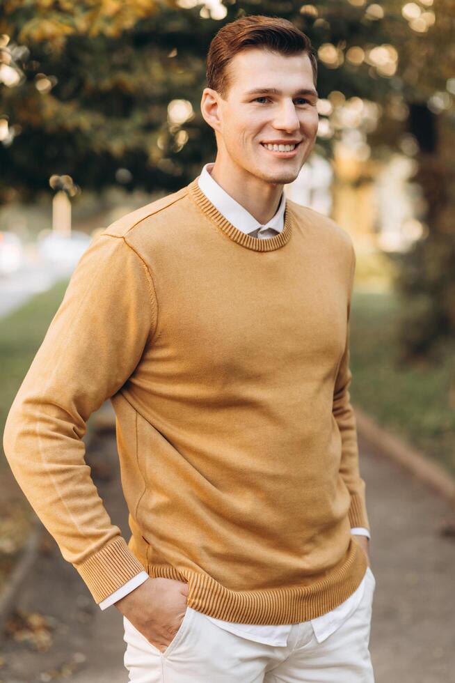 Modern handsome smiling man in yellow and white clothes posing in the park at sunset photo