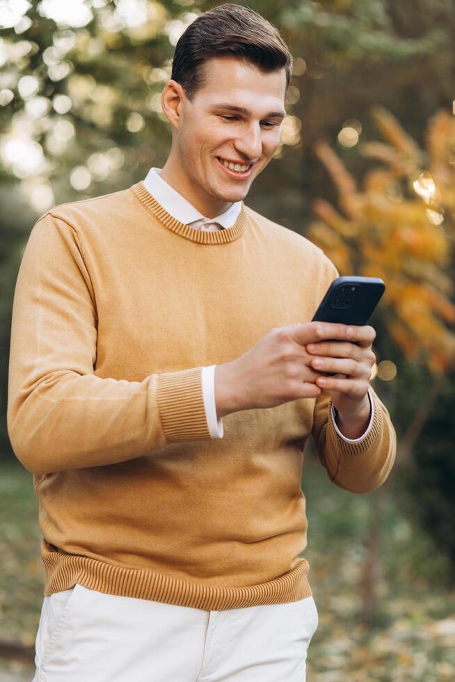 Modern handsome smiling man in yellow and white clothes talking on the phone in the park at sunset photo