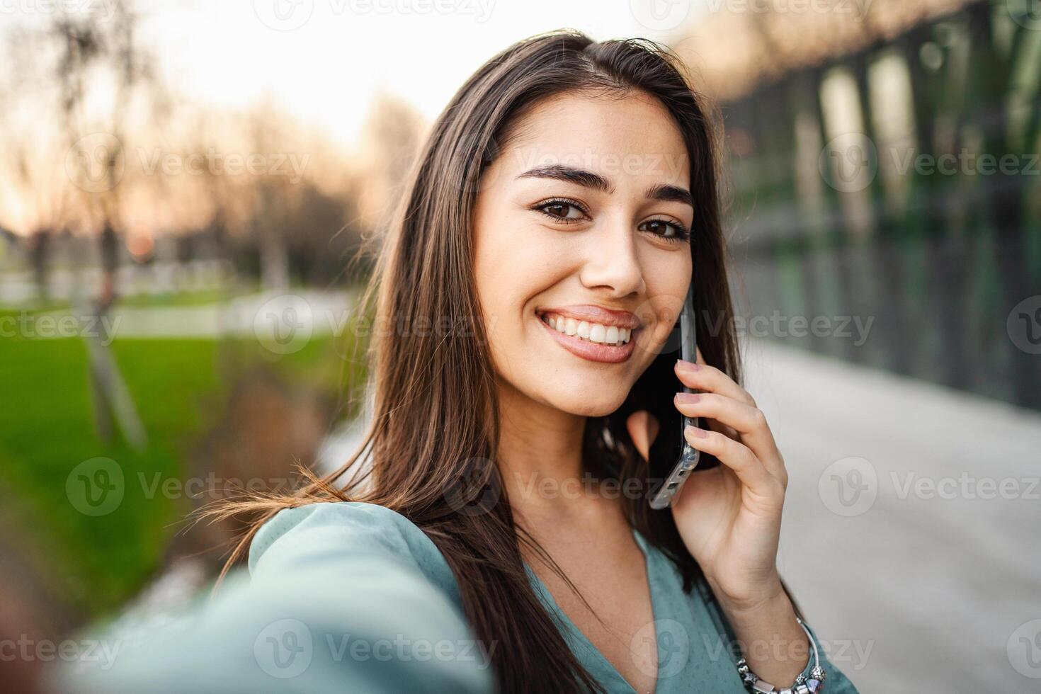 Selfie of smiling young brunette girl using mobile phone outdoors photo