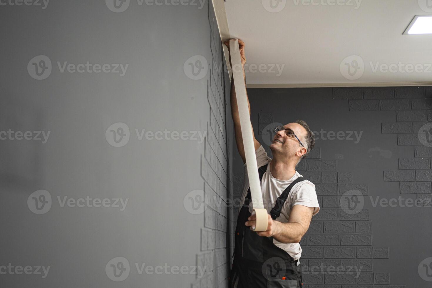 Man sticks protective tape on the wall before painting photo