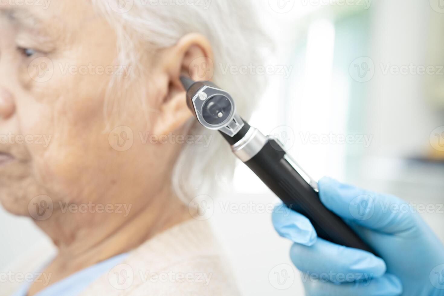 Otolaryngologist or ENT physician doctor examining senior patient ear with otoscope, hearing loss problem. photo
