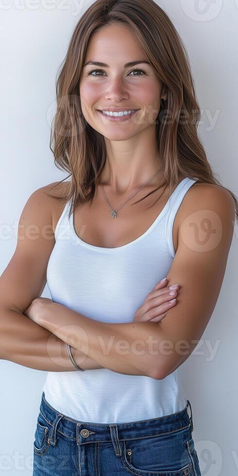 Smiling woman in a white tank top poses confidently against a light wall photo