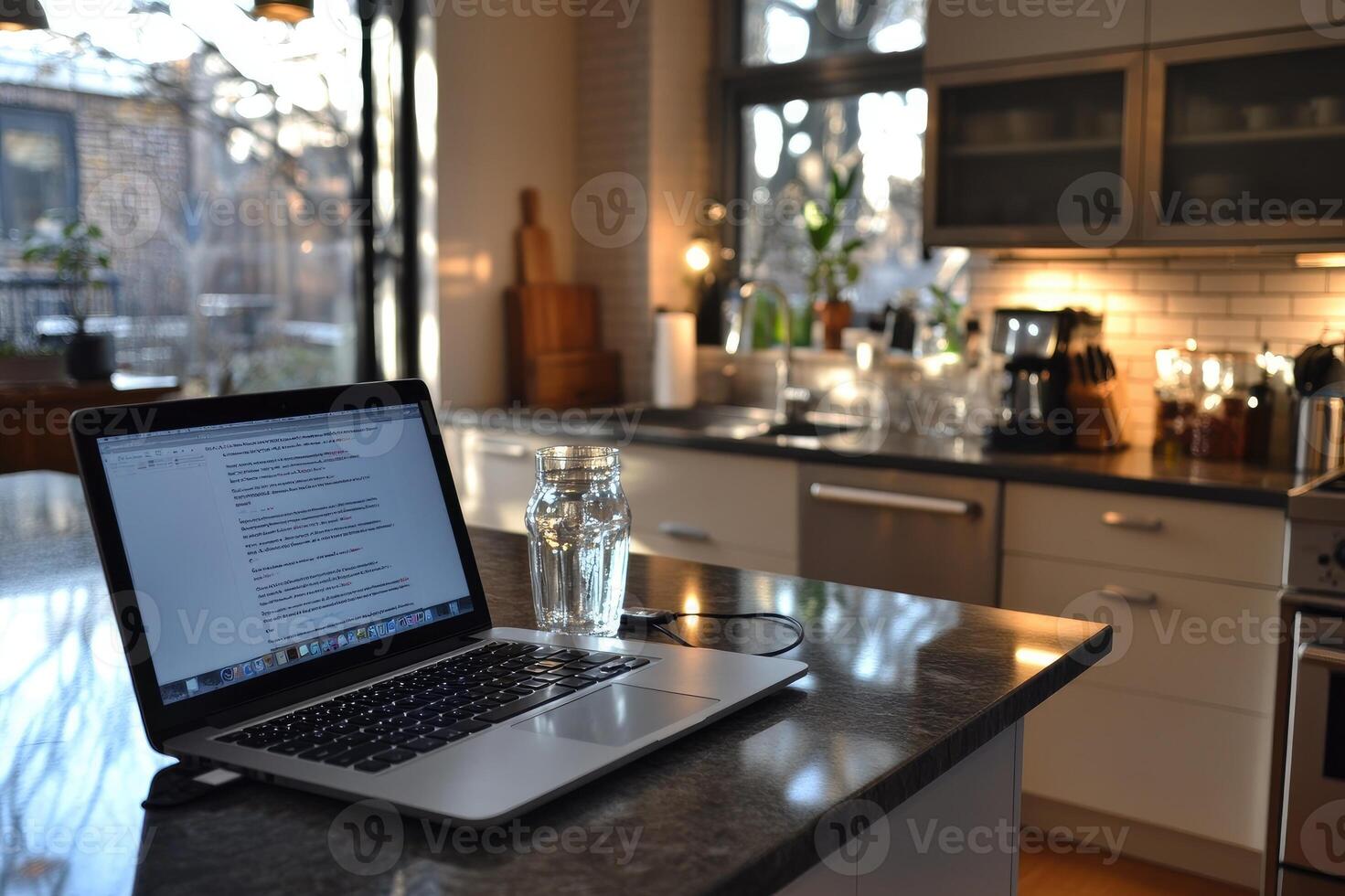 Laptop showing blank document open on kitchen counter with glass of water photo