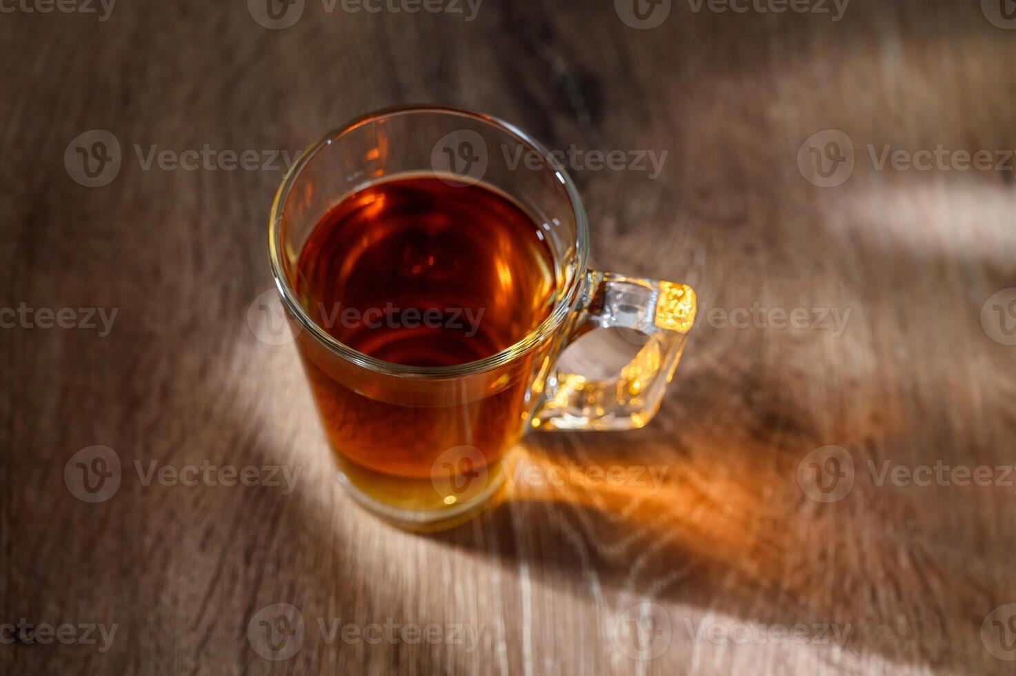 A clear glass cup of tea infused steaming on a wooden table photo