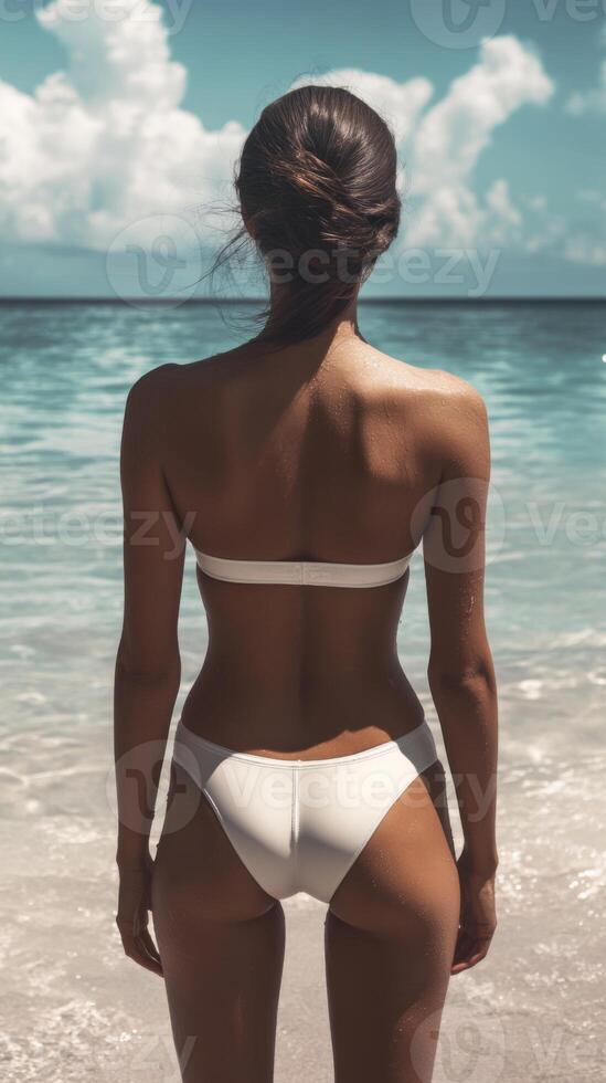 A Woman Dressed in a White Bikini Is Enjoying a Beautiful Beachfront View with Gentle Ocean Waves photo