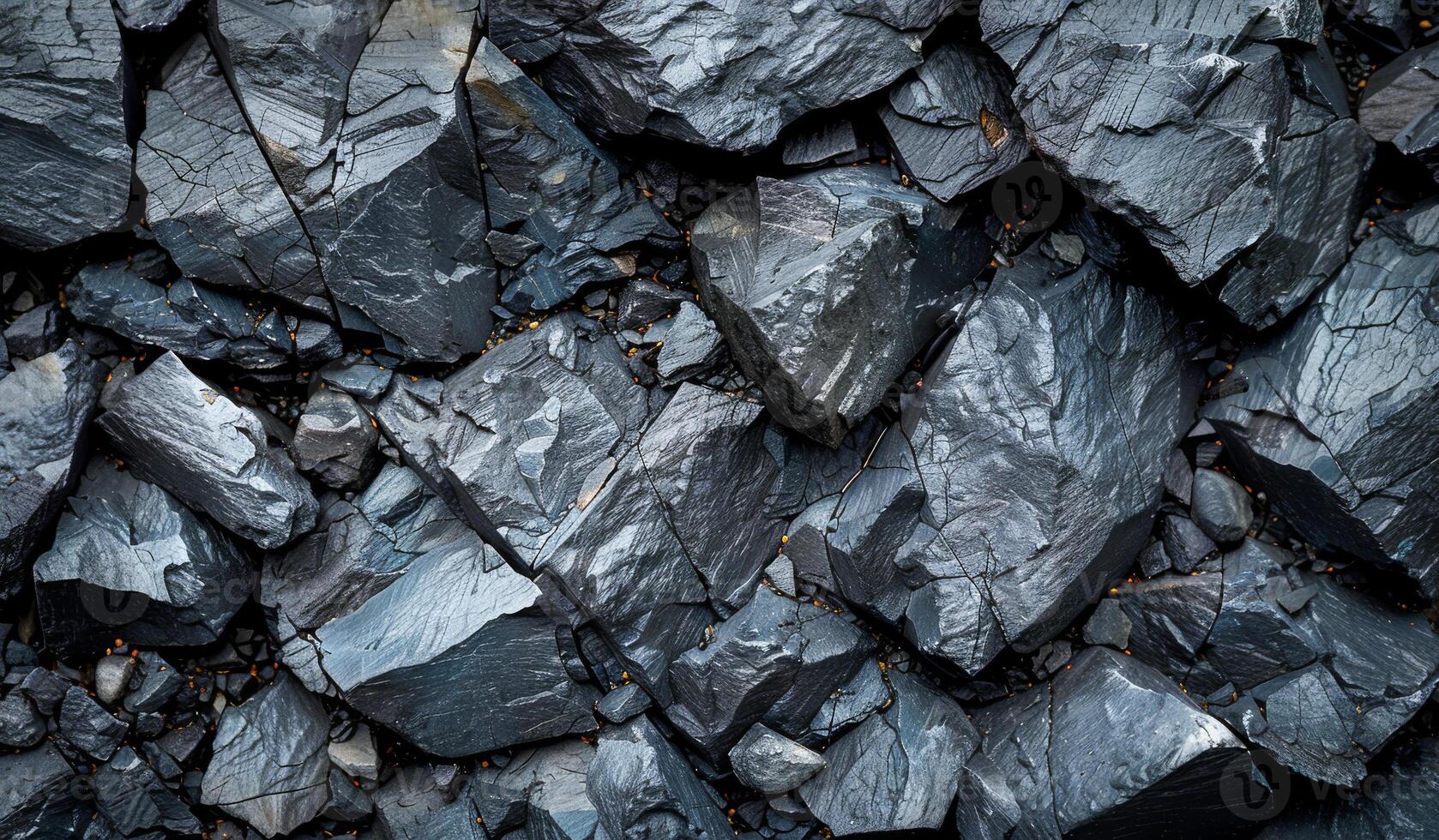 A close up of a pile of black rocks. The rocks are large and rough, with some of them having a shiny, metallic appearance. Scene is one of ruggedness and strength photo