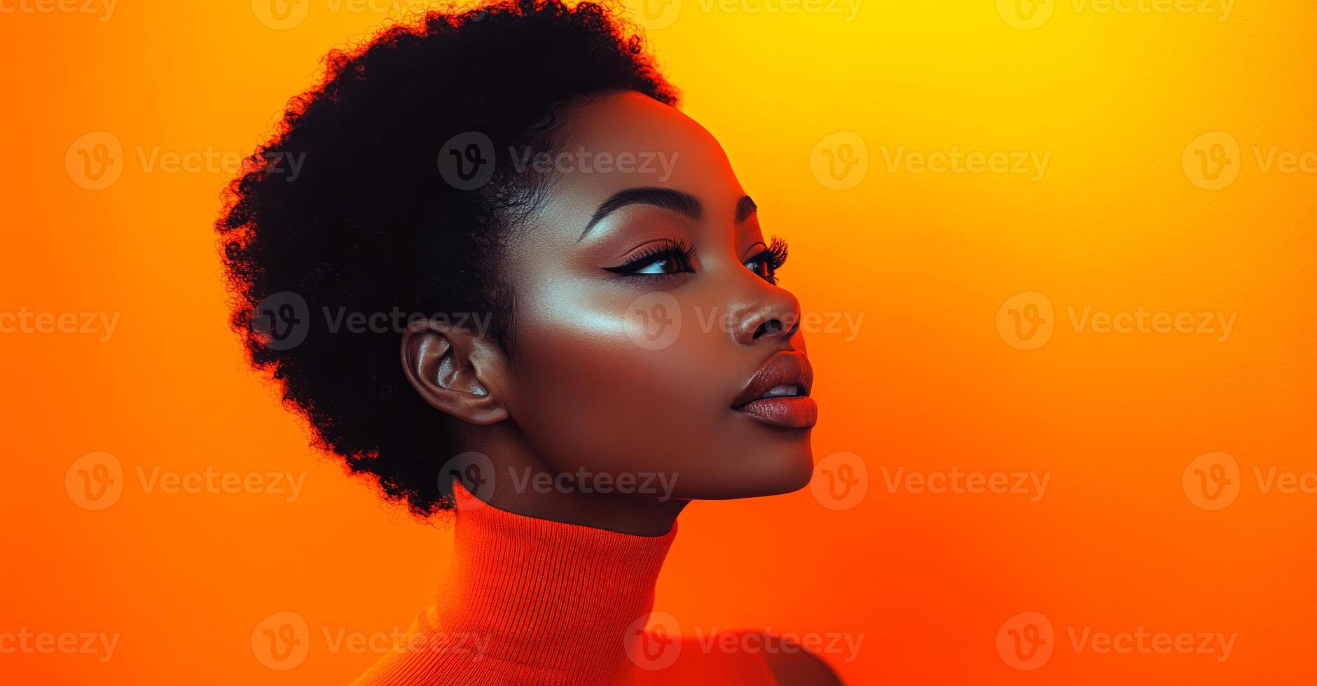 A woman with a short, curly black hair is wearing an orange sweater. She has a bright, glowing look on her face photo