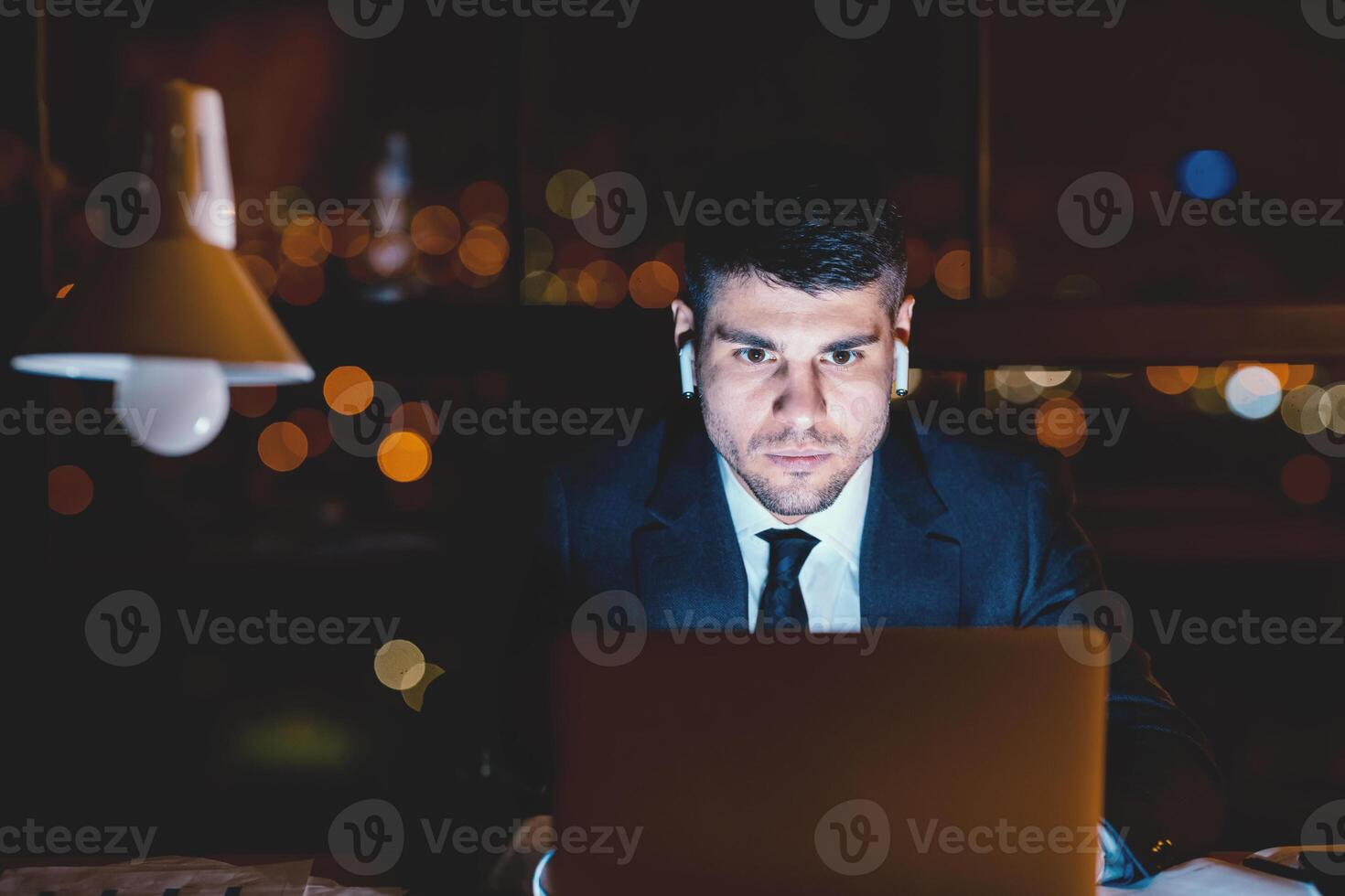 Concentrated Business Guy At Laptop Working Wearing Earbuds Overnight Sitting Alone In Modern Office. Copy Space, Selective Focus photo