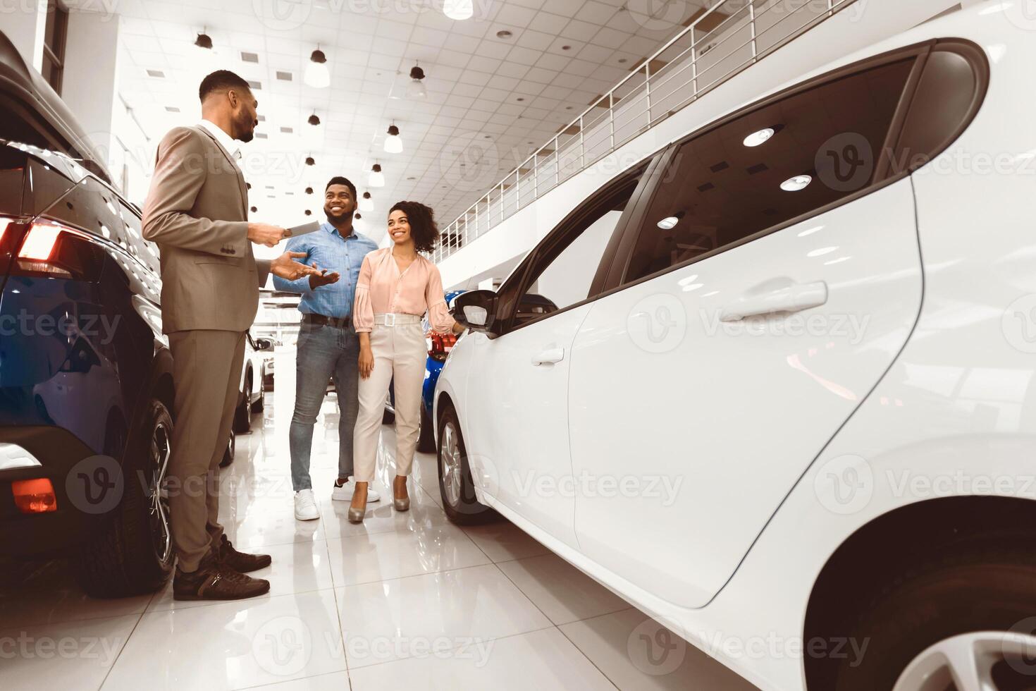 Car Sales. African American Spouses Buying New Car Choosing Auto With Seller Man In Luxury Automobile Dealership Center. photo