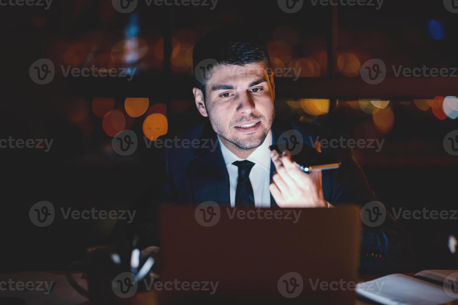 Busy Entrepreneur Using Smartphone Voice Assistant Working On Laptop In Modern Office Late At Night. Selective Focus photo