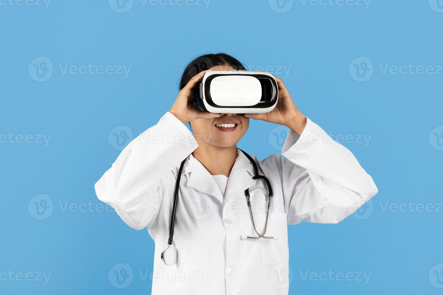 A medical professional Asian lady smiles while wearing a virtual reality headset. The background is a vibrant blue, highlighting the innovative use of technology in healthcare. photo