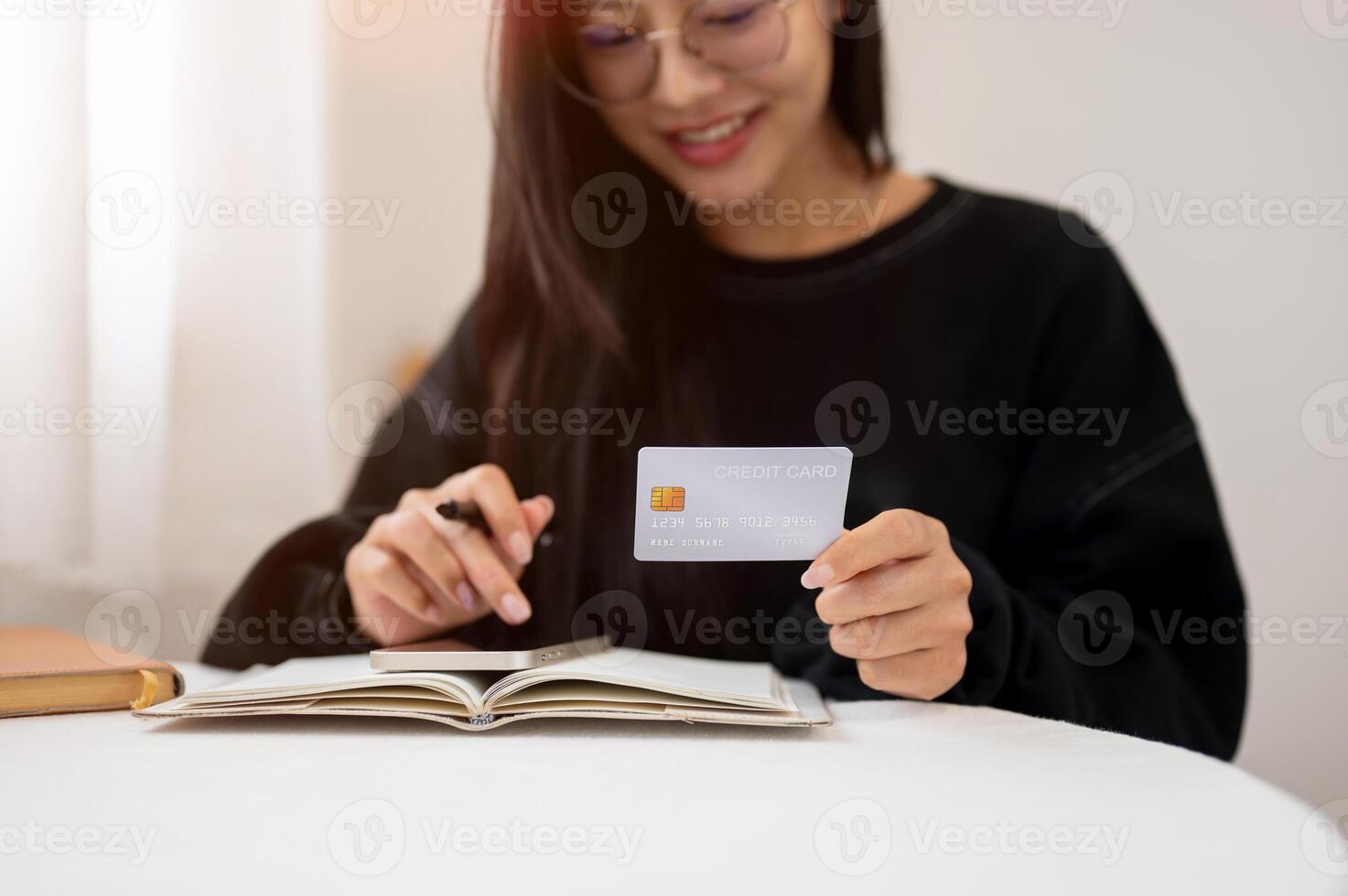 A cropped image of a woman using her phone and holding a credit card while planning her finances. photo