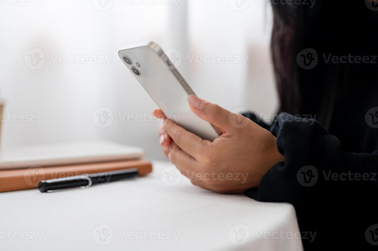 A close-up of a woman in a black sweater using her smartphone while sitting at a table indoors. photo