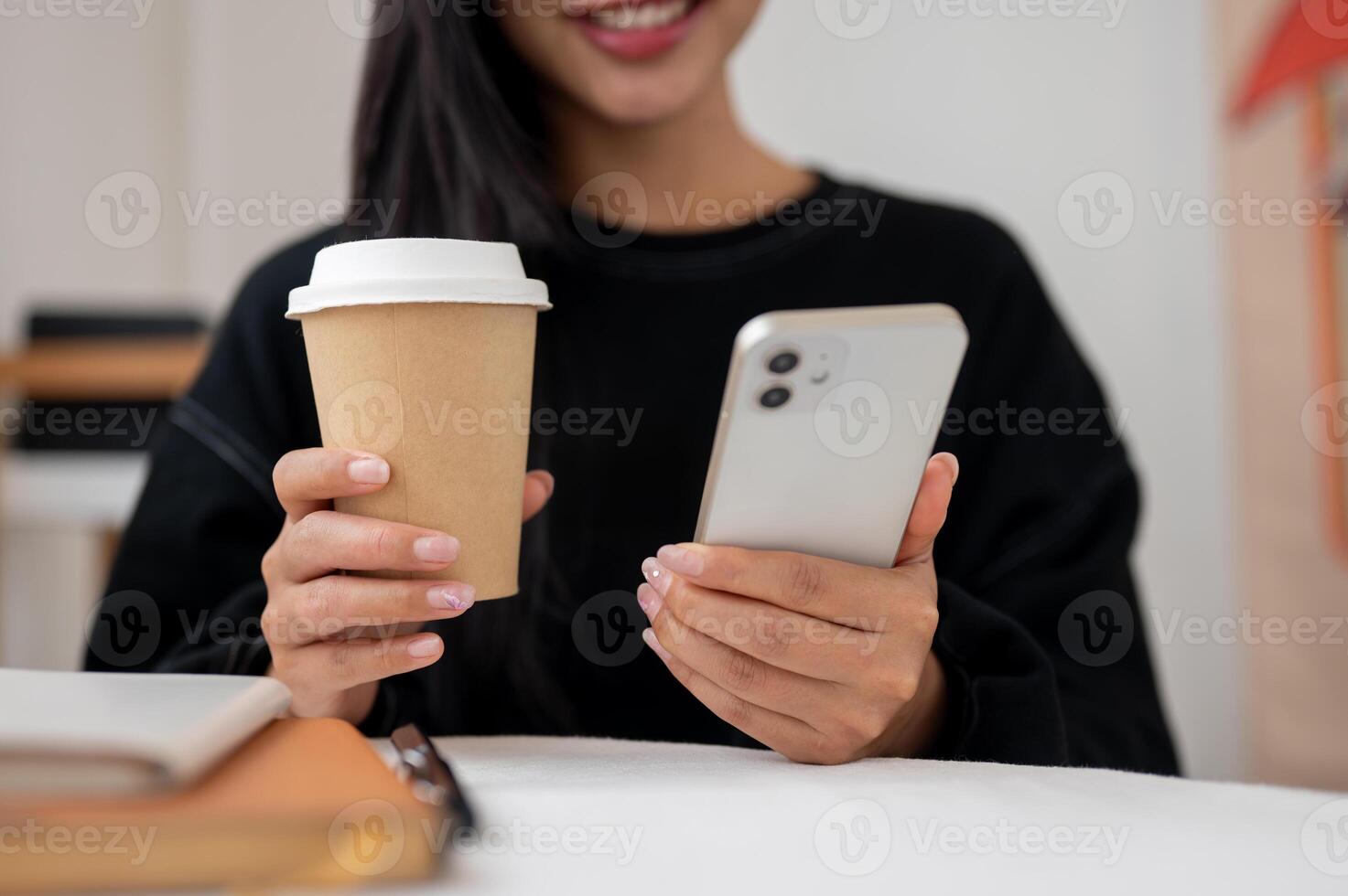 Close-up of a woman enjoying coffee while reading text on her phone at a table indoors or in a cafe. photo