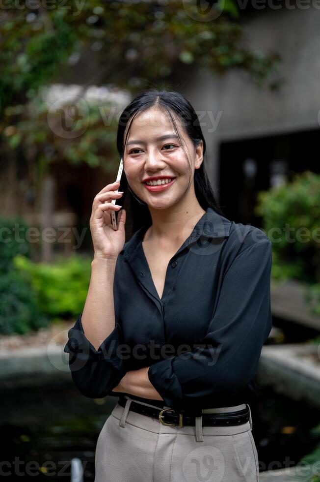 A charming Asian businesswoman is having a conversation on the phone while relaxing in a garden. photo