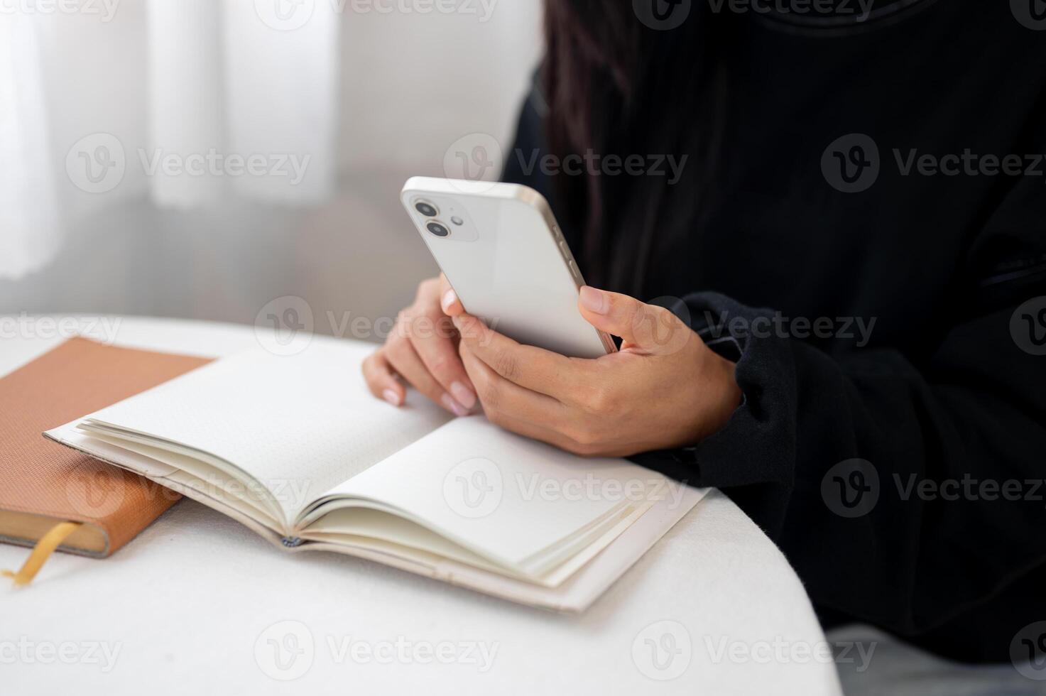 A close-up of a woman in a cozy sweater using her smartphone while reading at a table indoors. photo
