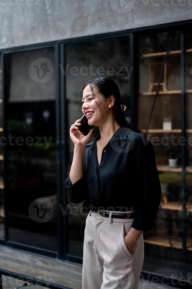 A confident Asian businesswoman is having a conversation on the phone while standing in her office. photo