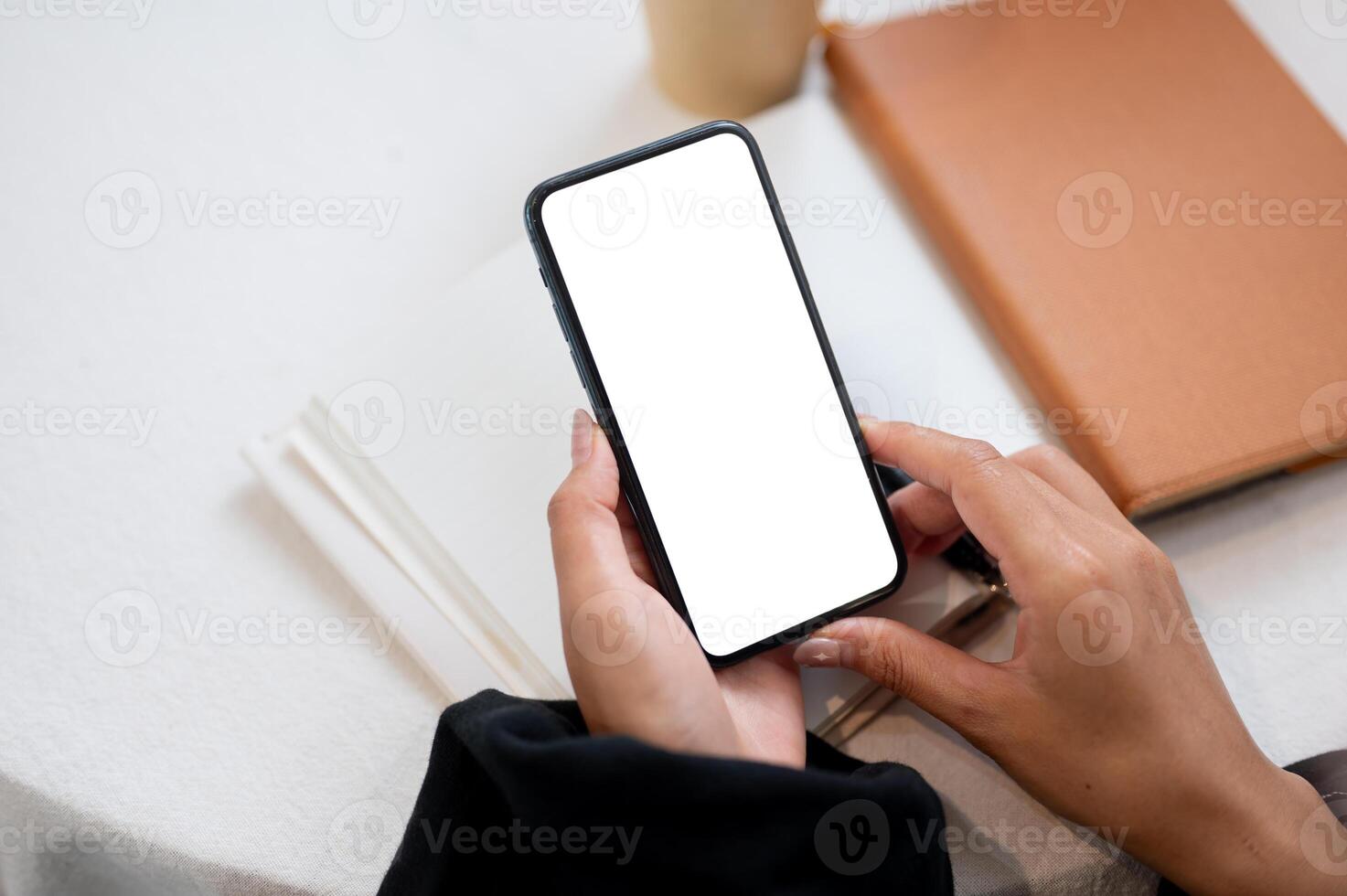 A close-up of a woman's hand holding a smartphone with a white screen mockup over a table. photo