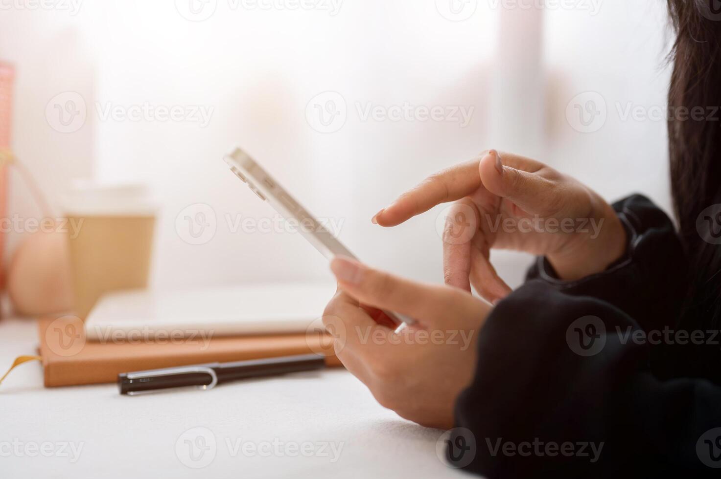 A close-up of a woman in a black sweater using her smartphone while sitting at a table indoors. photo