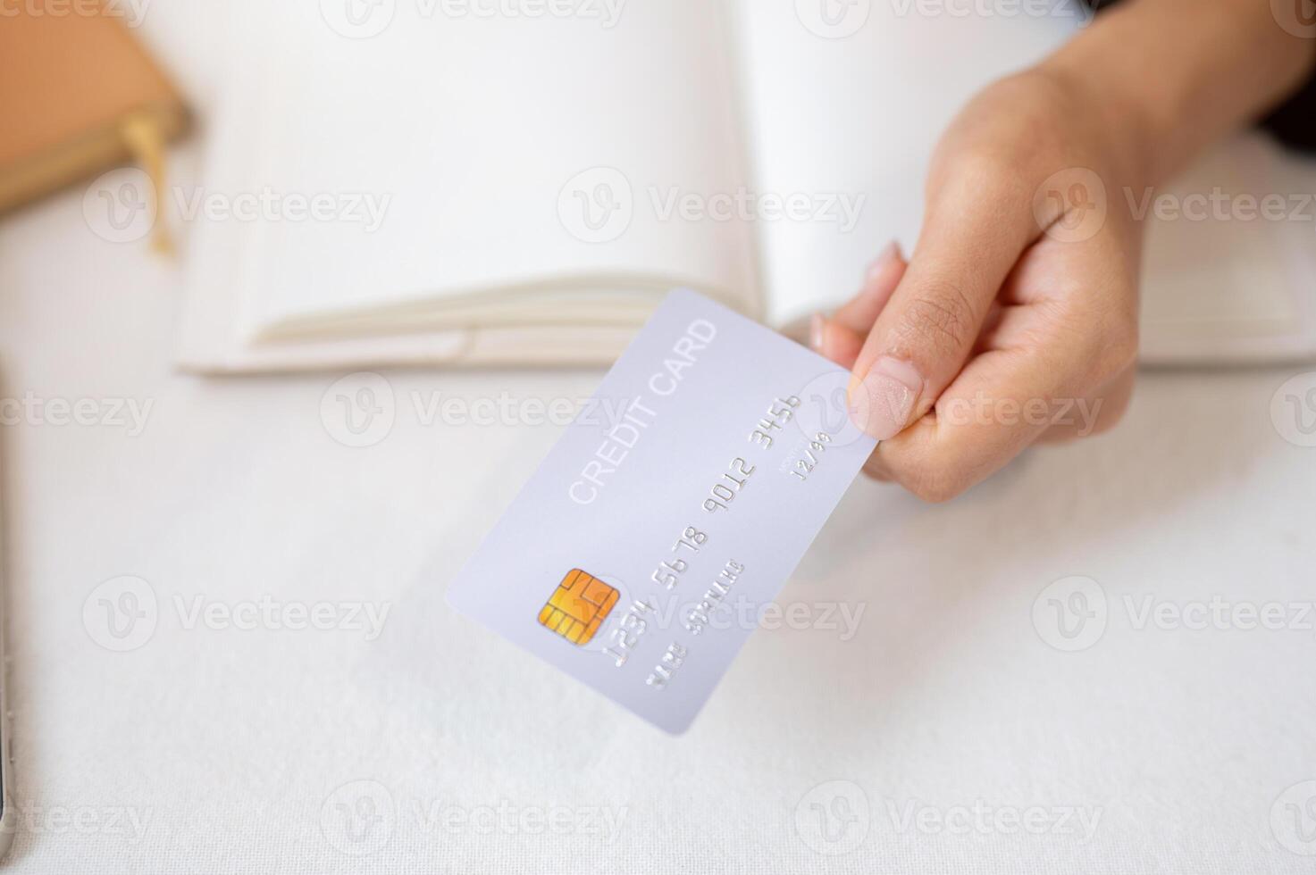 A top view of a woman's hand holding a credit card over a white table. photo