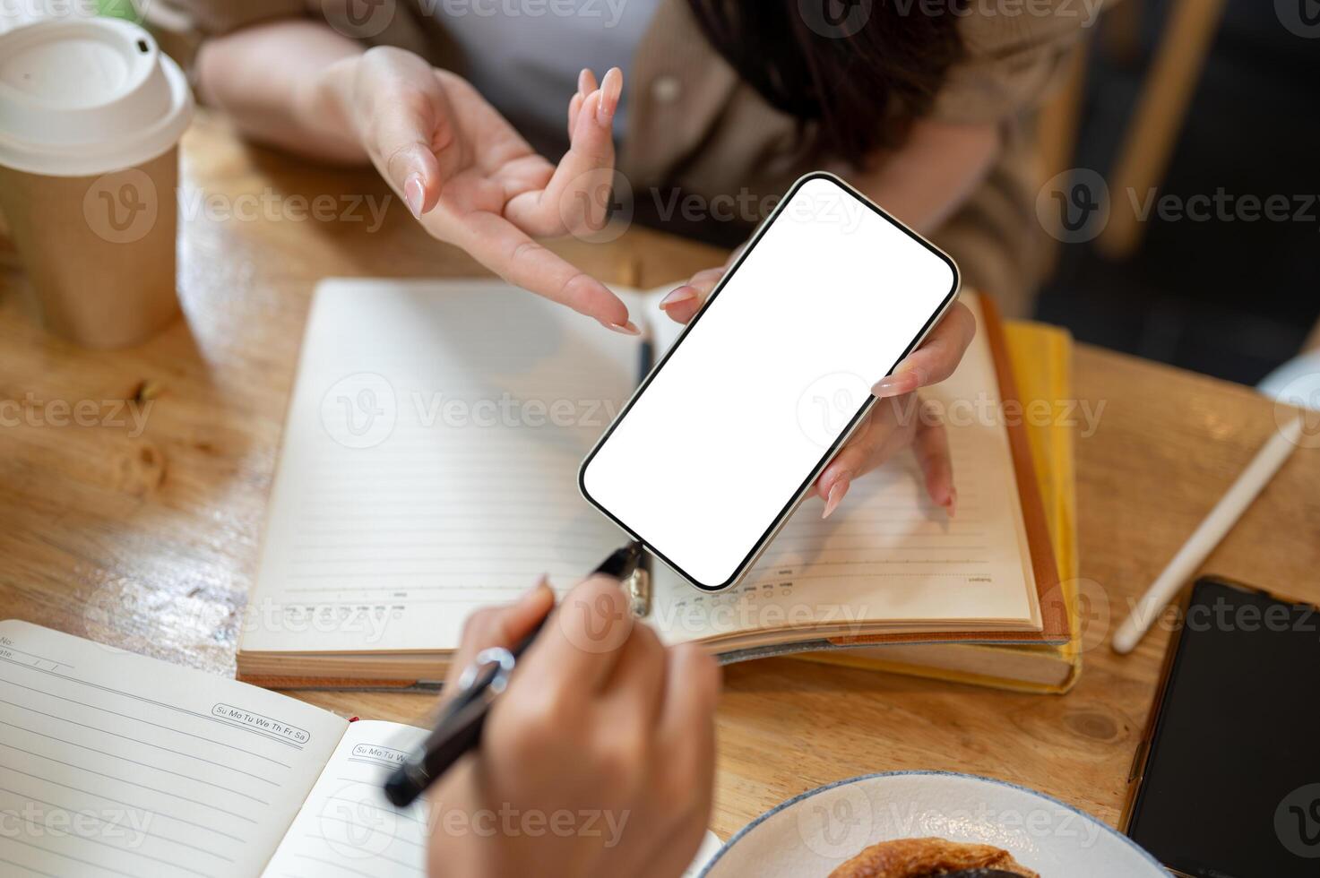 A close-up of a woman showing her smartphone to a friend while discussing work, at a table indoors. photo