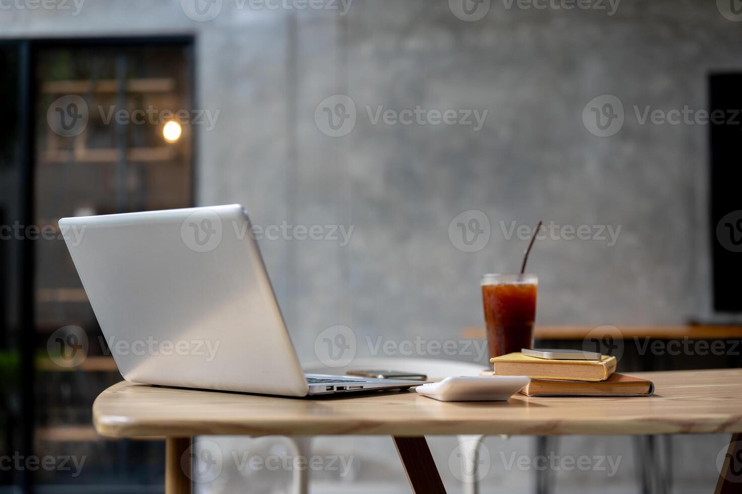 A laptop, a calculator, books, and a glass of iced coffee on a table in a modern loft coffee shop. photo
