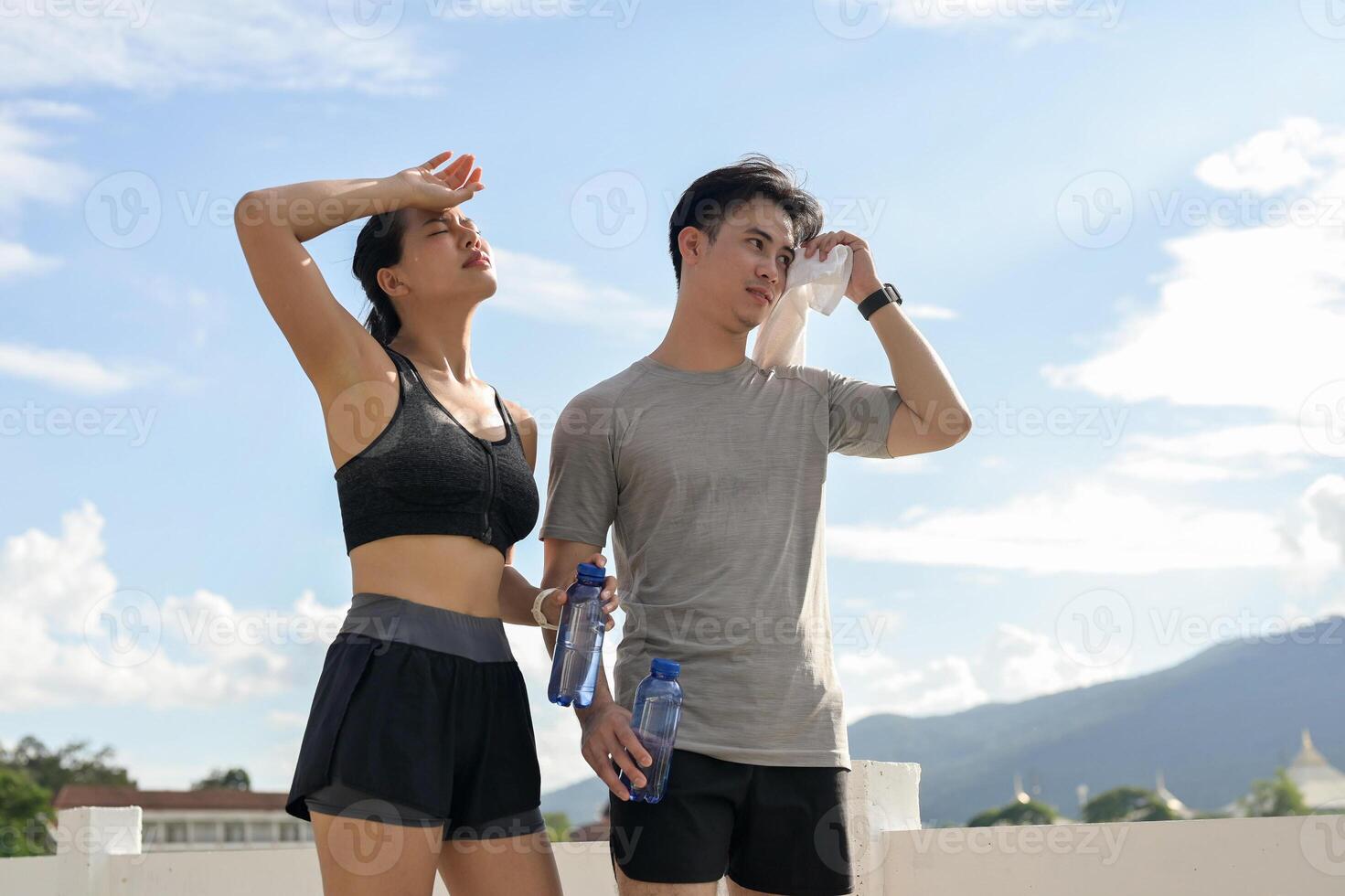 A tired, sweaty couple in sportswear is resting together after a long run in a park on a sunny day. photo