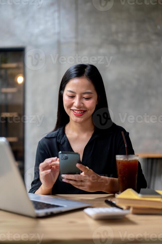 An attractive Asian woman is using her smartphone while sitting at a table in a coffee shop. photo